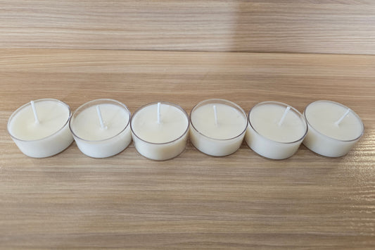 Six white tealight candles in holders lined up on a wooden surface